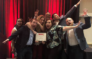 a group of people stand together with their arms raised celebrating an award