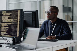 Black man in glasses looks at his computer seriously