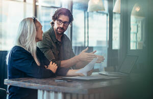 a man sits at a table with his hands raised talking to a woman