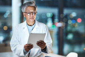 an older woman doctor in a white while analyzes a tablet