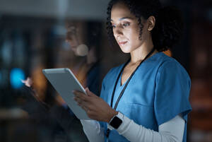 a nurse in blue scrubs reads a tablet