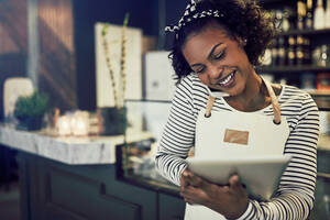 a woman in a striped shirt and apron makes a call on her cellphone while holding a tablet